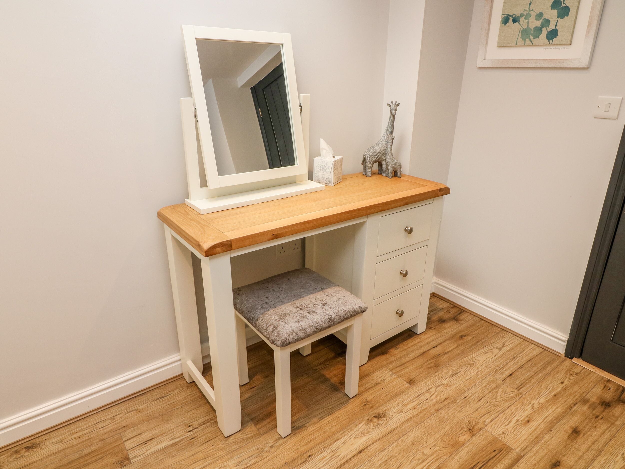 Une coiffeuse blanche avec un plateau en bois, un miroir et un petit banc.