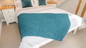 Un lit bien fait, agrémenté d’un plaid turquoise, de deux oreillers et de deux lampes de chevet.