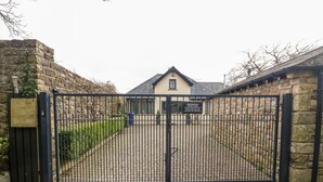 Une entrée fermée par un portail mène à une propriété portant l’inscription « 5 Lake House », avec un panneau d’avertissement, un mur de pierres et une allée pavée.