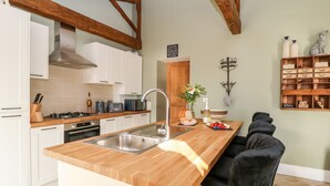 Una cocina con vigas de madera, armarios blancos, encimera de madera, un lavamanos y una barra desayunadora.