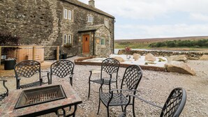 A stone building with a wooden door, outdoor seating with metal chairs, and a fire pit. - Skyfell (Skipton)