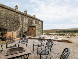 A stone building with a wooden door, outdoor seating with metal chairs, and a fire pit.