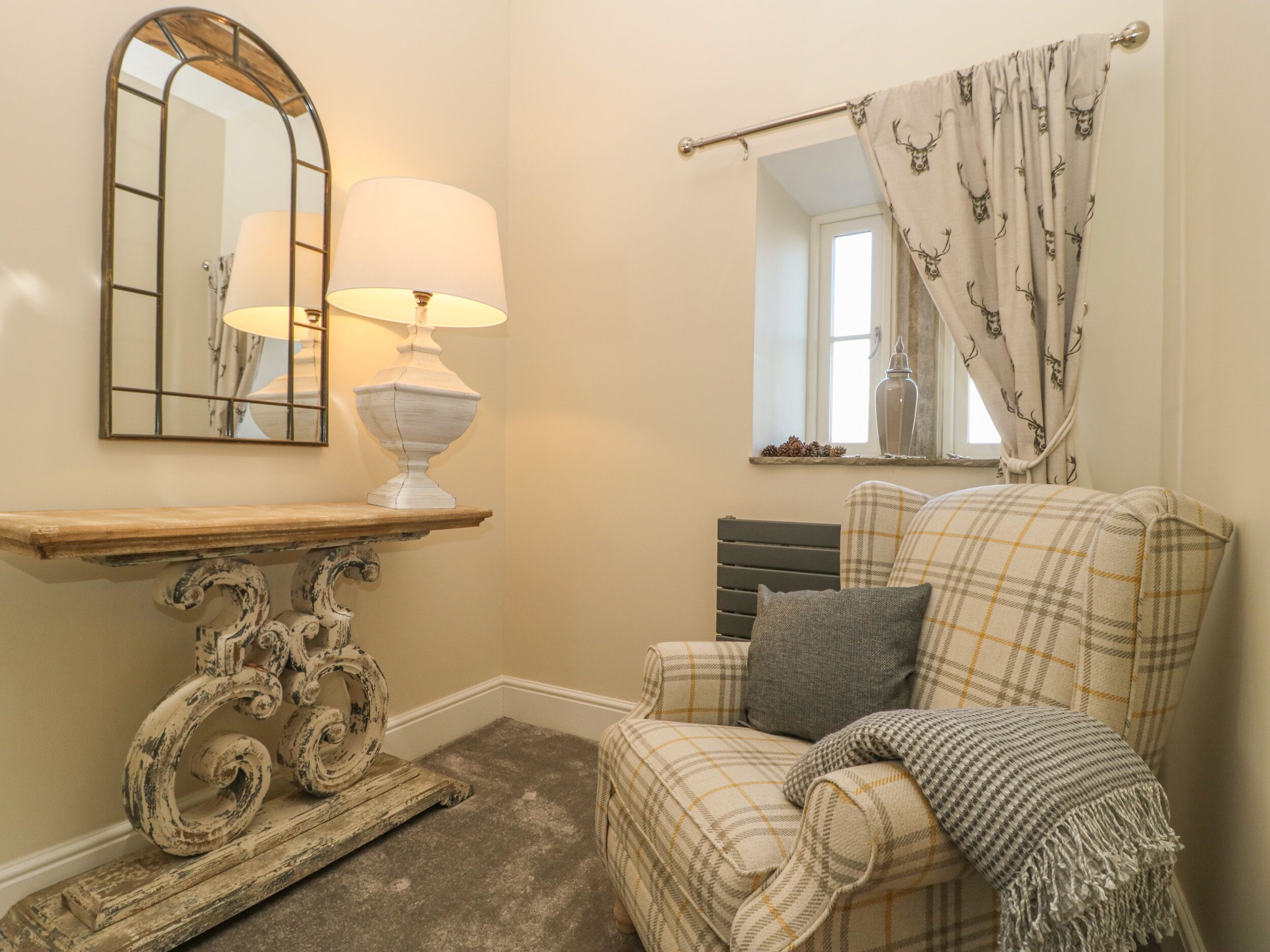 A cozy room with a plaid armchair, a white lamp, a mirror, and a window with curtains.