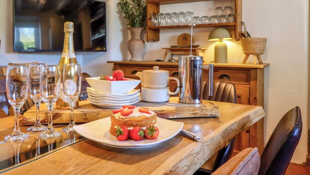 A dining table with a cake, glasses, and a bottle, surrounded by chairs and a wooden table. - Cefn Nannau (Corwen)