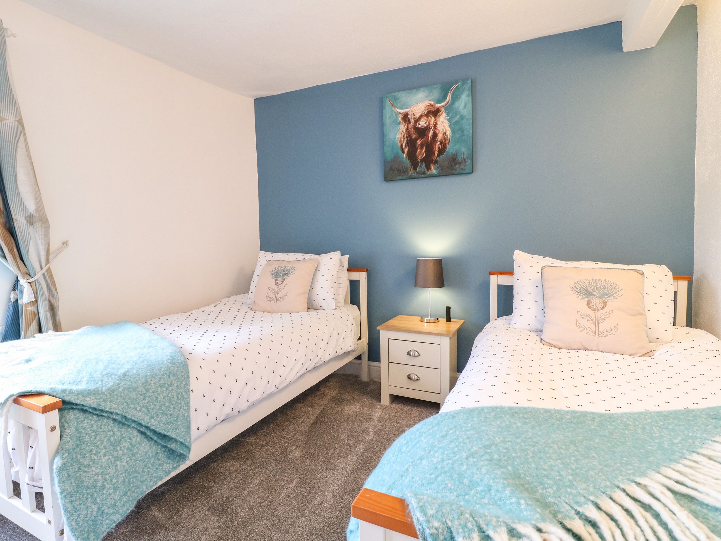 A bedroom with two single beds, a nightstand with a lamp, and a wall-mounted painting of a bull.