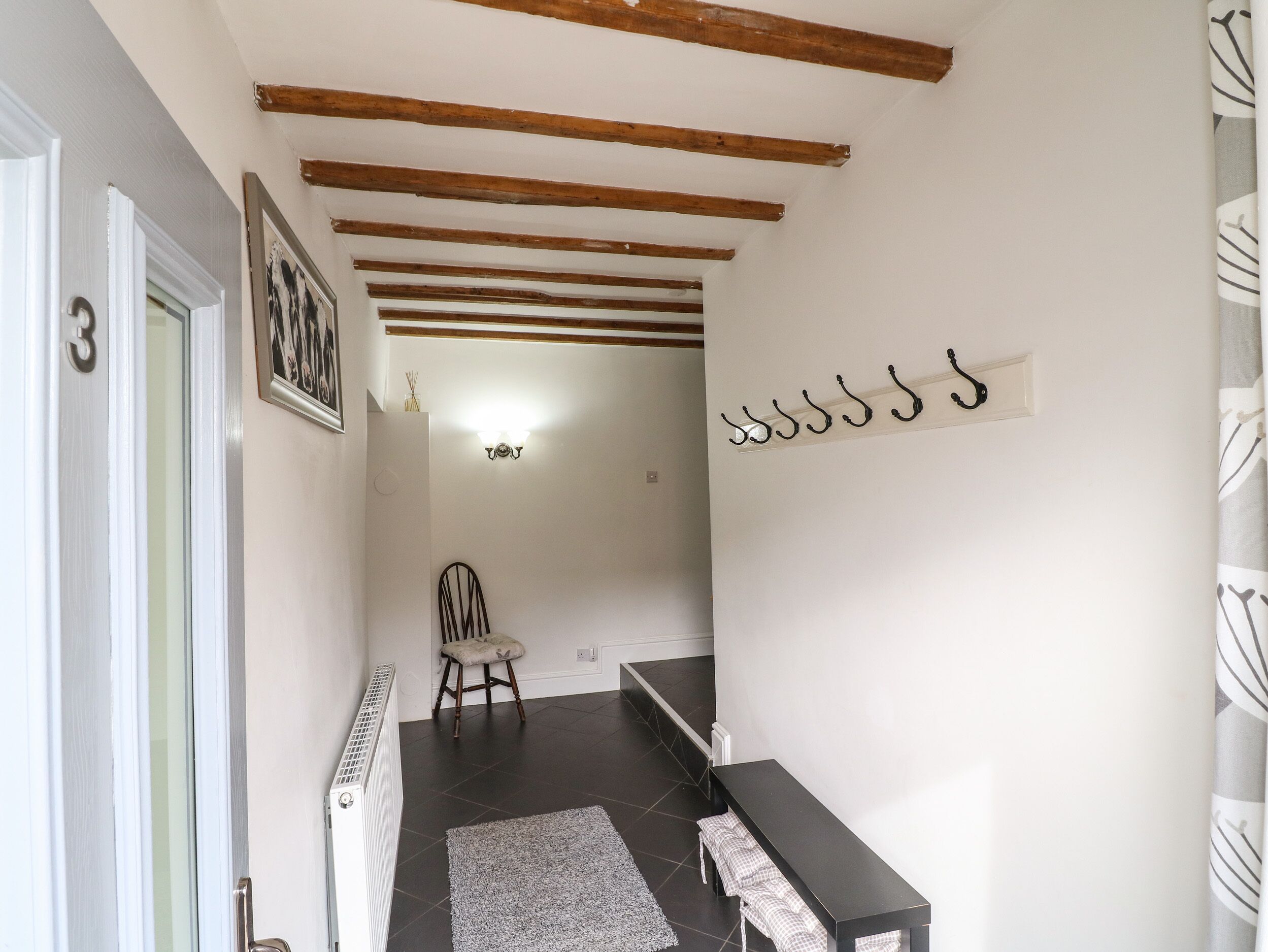 Un couloir avec un radiateur, une chaise, un banc et un porte-manteau fixé au mur.