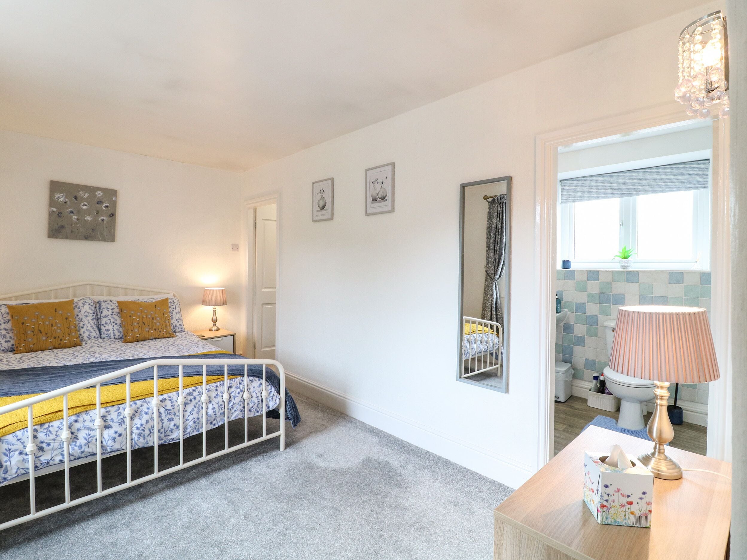 Een slaapkamer met een bed, nachtkastje, lamp en een spiegel.