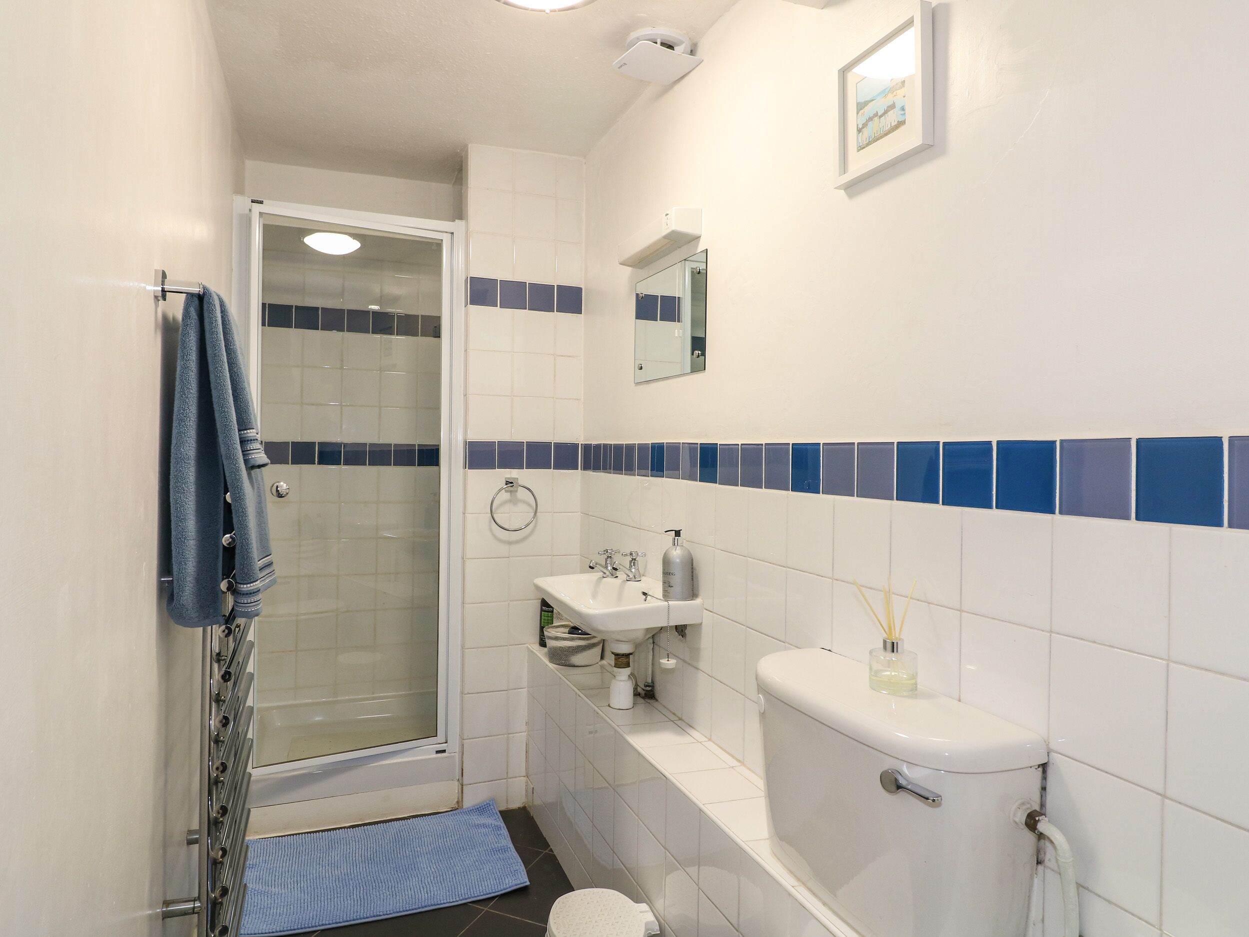 A bathroom with a glass shower enclosure, a sink, a toilet, and a blue-tiled accent wall.