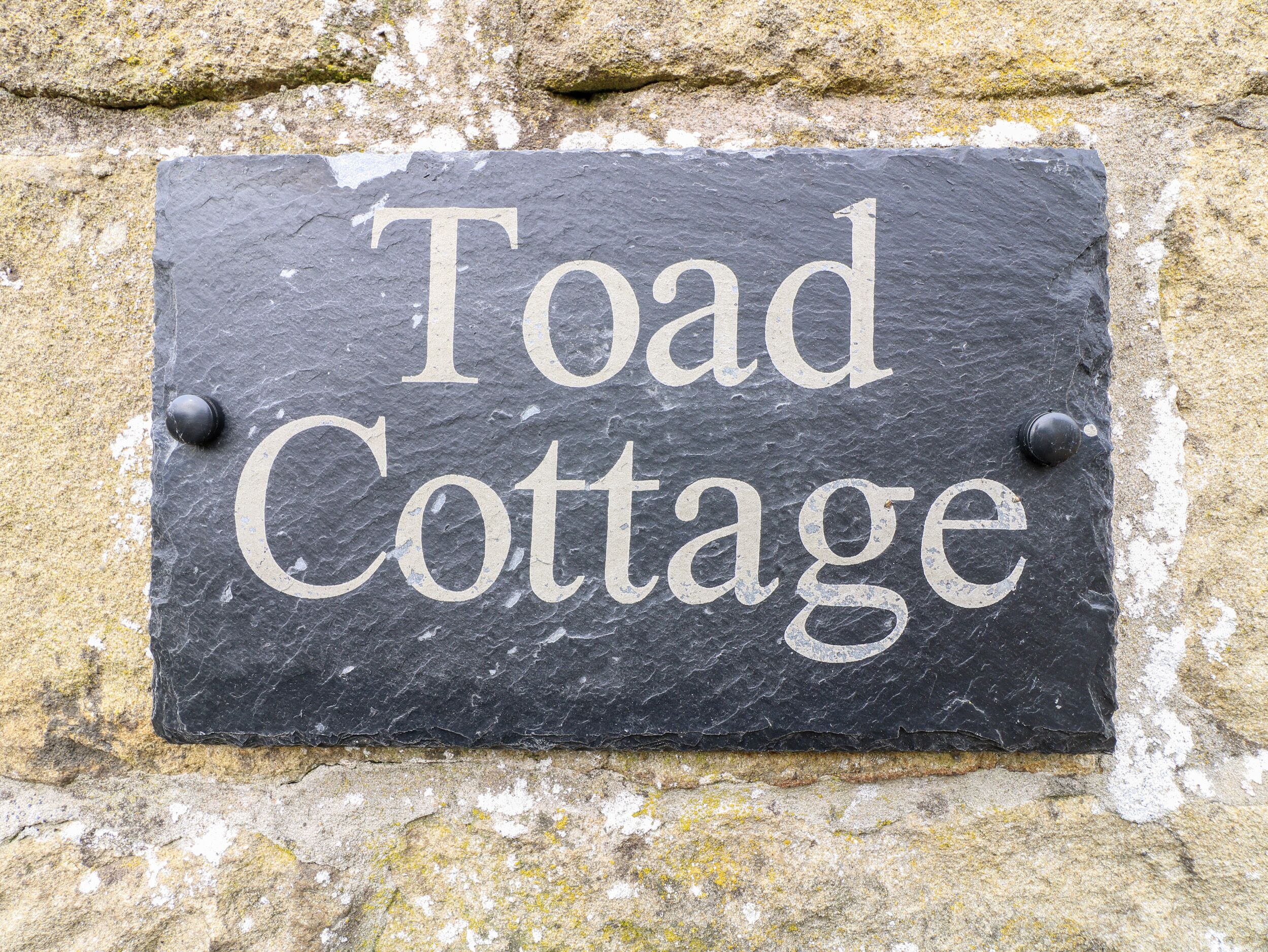 En skiferplade med teksten "Toad Cottage" monteret på en stenvæg.