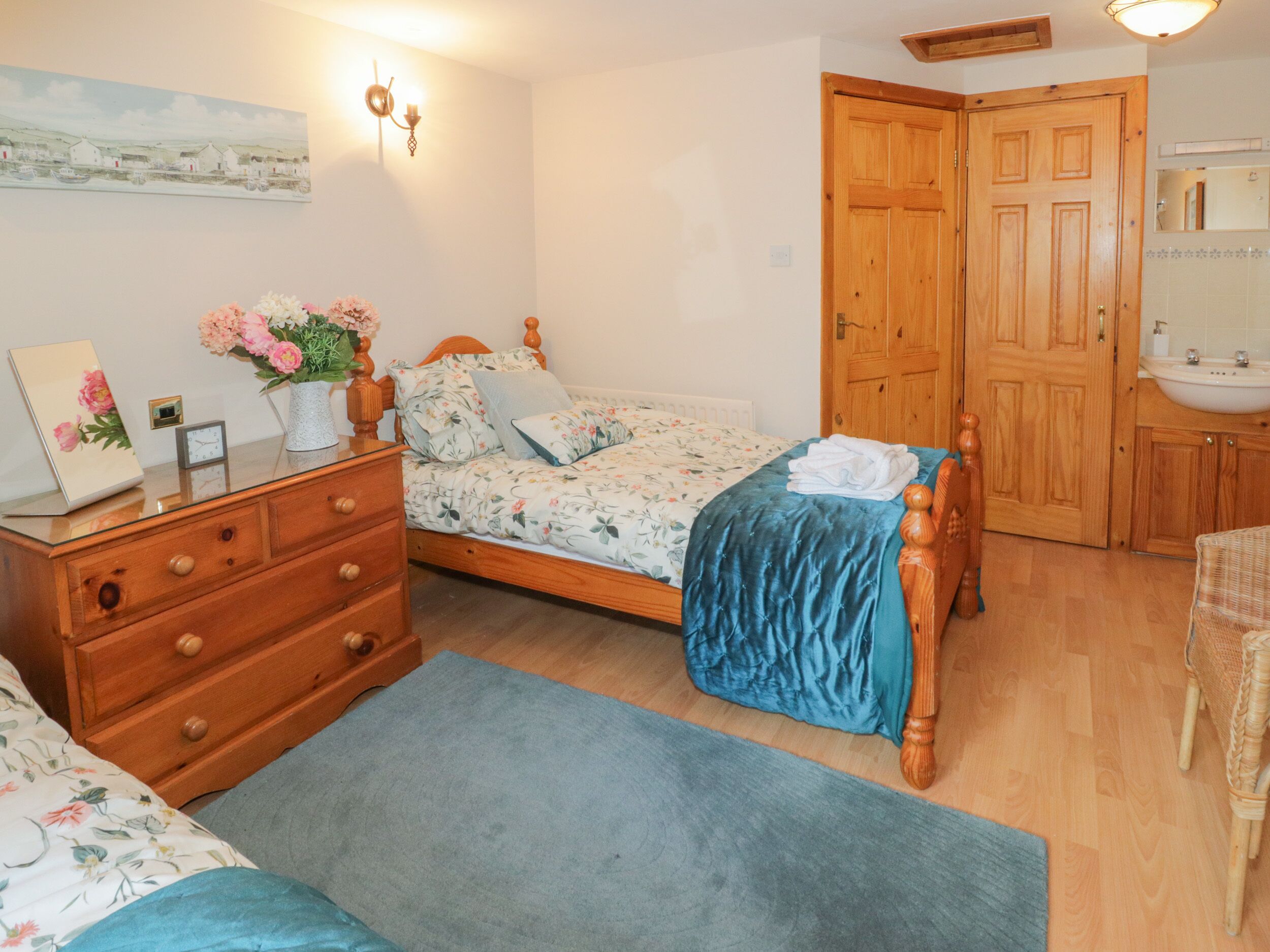 A bedroom with a bed, dresser, bedside table, and a wall-mounted lamp.