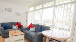 Una sala de estar moderna con un sofá gris, una mesa de centro de madera y una mesa redonda con cojines marrones. Hay dos cojines, uno rojo y otro azul, sobre el sofá.