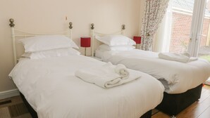 Ein Hotelzimmer mit zwei Einzelbetten, jeweils mit weißer Bettwäsche und Kissen, einer roten Nachttischlampe und einem blumigen Vorhang.