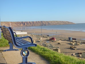 A bench overlooking a beach with a rocky embankment in the background. - Arbour Retreat (Filey)