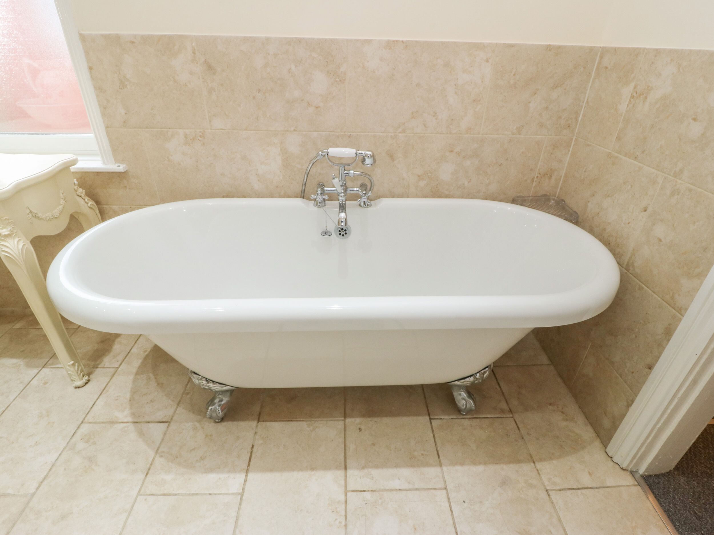 A white freestanding bathtub in a bathroom with beige tiles.