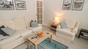 A living room with a beige sofa, a wooden coffee table with fruit, a striped rug, and framed artwork on the wall. - Hazelmere Cottage (Worksop)