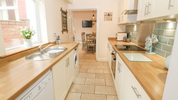 A compact kitchen with white cabinets, a dishwasher, and a wooden countertop. - Hazelmere Cottage (Worksop)