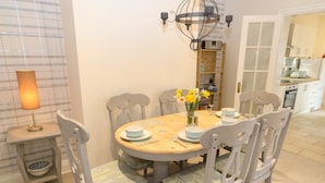 A dining area with a round table, six chairs, a chandelier, and a lamp. - Hazelmere Cottage (Worksop)