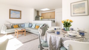 A modern living room with a sofa, dining table set with plates and cups, and a kitchen in the background. - Sea Point (Exmouth)