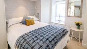 A modern bedroom with a bed, a bedside table with a vase of flowers, and a window with a view. - Sea Point (Exmouth)