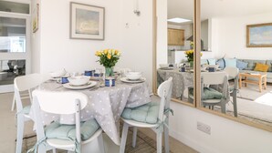 A dining area with a table set for four, chairs with cushions, a vase with flowers, and a large mirror reflecting the room. - Sea Point (Exmouth)