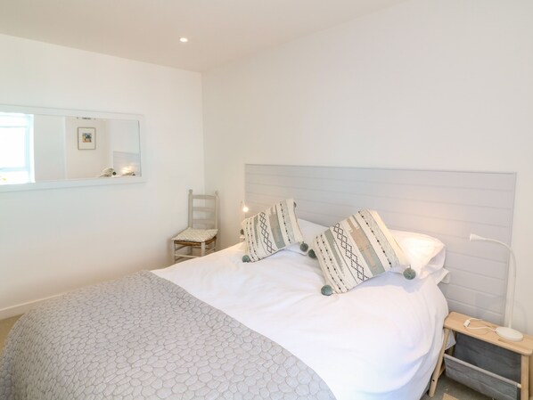 A neatly arranged bedroom with a bed, a bedside table, a chair, and a nightstand.