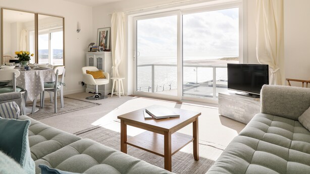 A modern living room with a sofa, a coffee table, a TV, and a balcony with a view of the sea. - Sea Point (Exmouth)