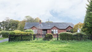 A brick house with a sloped roof, surrounded by a well-maintained lawn and hedges. - The Alders (Llanfyllin)