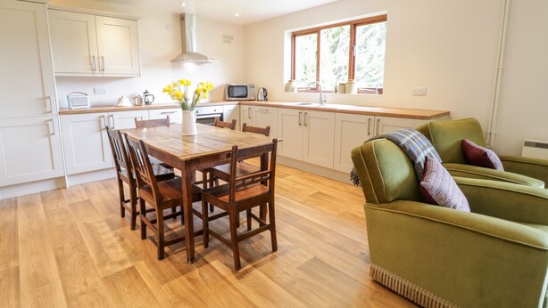 A modern kitchen with white cabinets, a wooden dining table, and a green sofa. - The Alders (Llanfyllin)