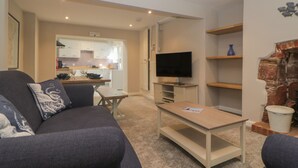 A living room with a sofa, a coffee table, a TV, and a kitchen in the background.