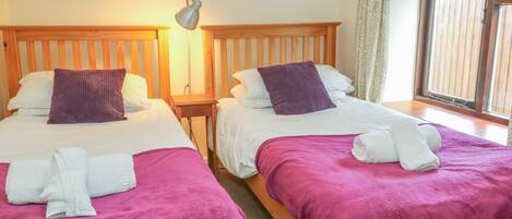Two single beds with wooden headboards, white linens, purple pillows, and a purple blanket.