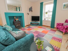 Una sala de estar con un sofá verde azulado, un sillón rosa, un televisor, una chimenea y una alfombra colorida.