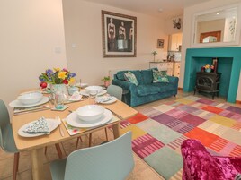 Un comedor con una mesa lista para cuatro personas, un sofá, una chimenea y una alfombra colorida.