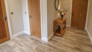 A hallway with wooden doors, a small wooden table with a vase of flowers, and a mirror on the wall. - Horsley Cottage (Consett)