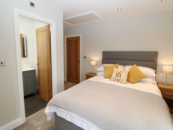 Une chambre à coucher comprenant un lit, des tables de chevet, une commode et une porte donnant sur une autre pièce.