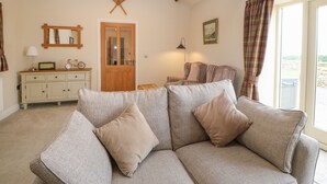 A cozy living room with a sofa, a wooden ceiling, a door, a mirror, and a window with curtains. - Horsley Cottage (Consett)