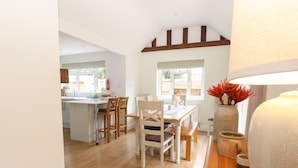 A bright kitchen with white cabinets, a wooden dining table with chairs, and a large window with a view of greenery. - The Lodge (Norwich)