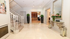 A spacious hallway with a staircase, a large mirror, and a console table with a vase of flowers. - Gleneagles (Ascot)