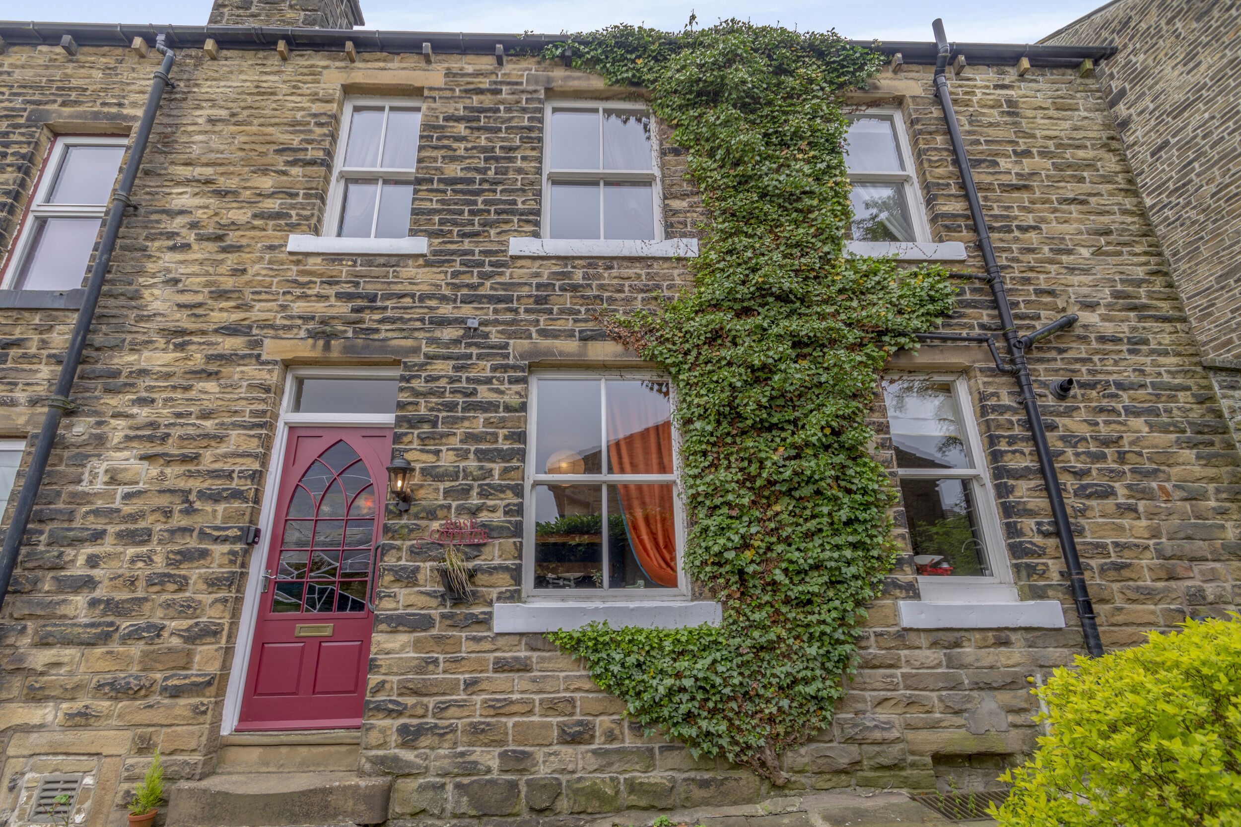 A stone building with a red door, multiple windows, and a vine-covered wall.