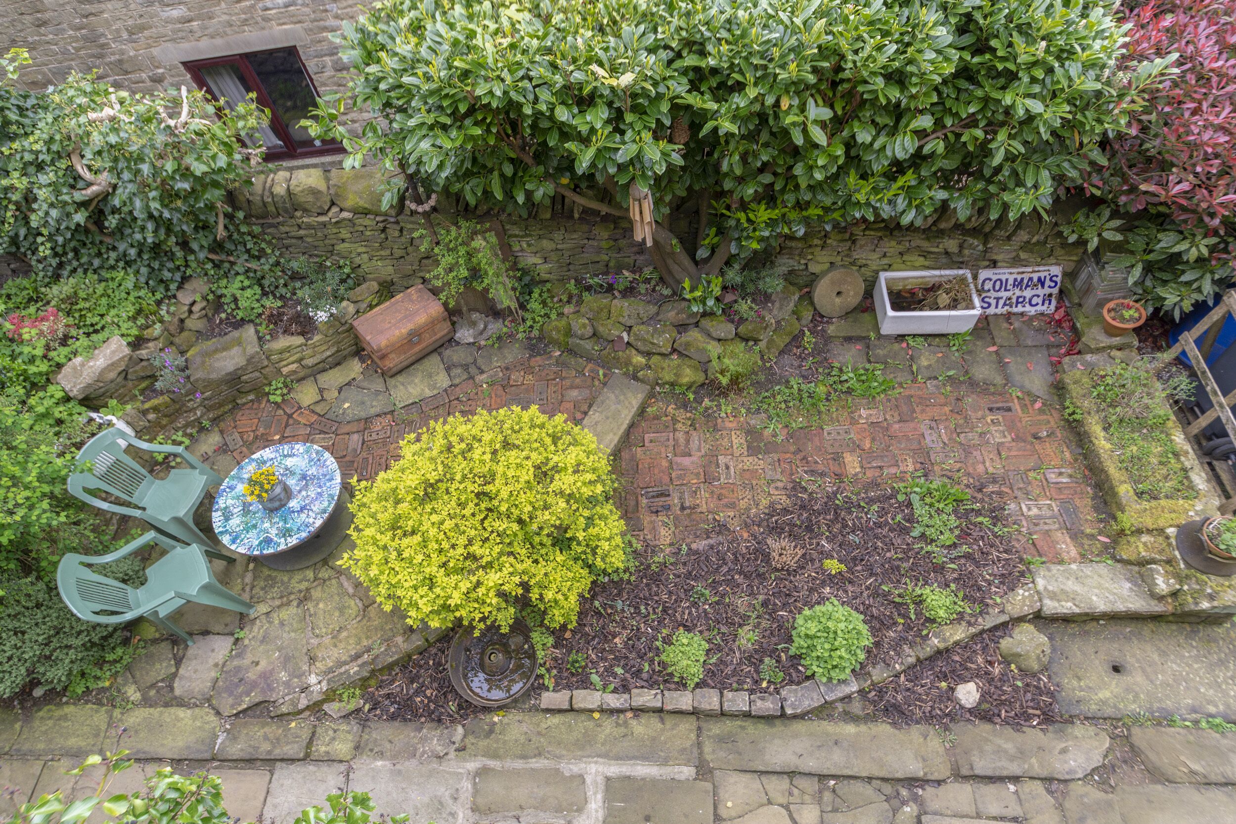A garden with a stone wall, a sign reading "Colman's Starch", and a table with chairs.