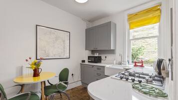 Una cocina compacta con encimera blanca, estufa y ventana con cortinas amarillas.
