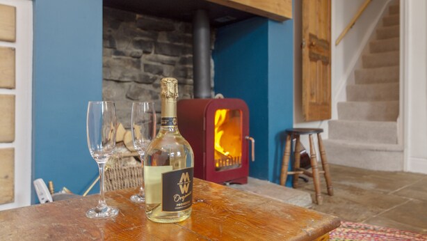 A bottle of whiskey and glasses on a wooden table in a room with a stone fireplace and a wooden staircase. - Rose Cottage (Keighley)