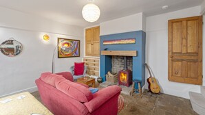 A cozy living room with a red sofa, a fireplace, a guitar, and a wooden door. - Rose Cottage (Keighley)