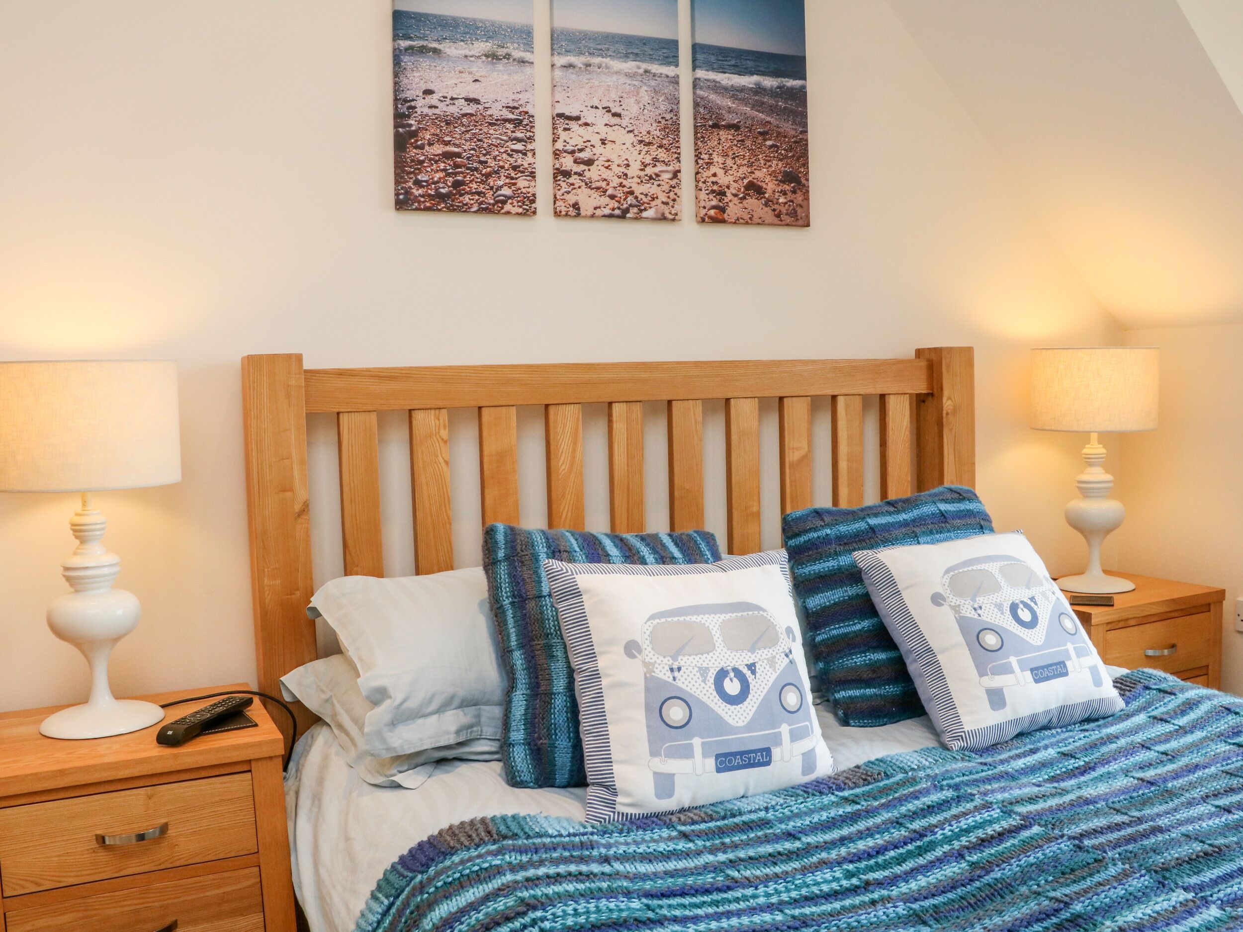 Une chambre à coucher avec une tête de lit en bois, deux tables de chevet avec des lampes, un lit avec une literie bleue et blanche, et un coussin sur le thème de la mer.