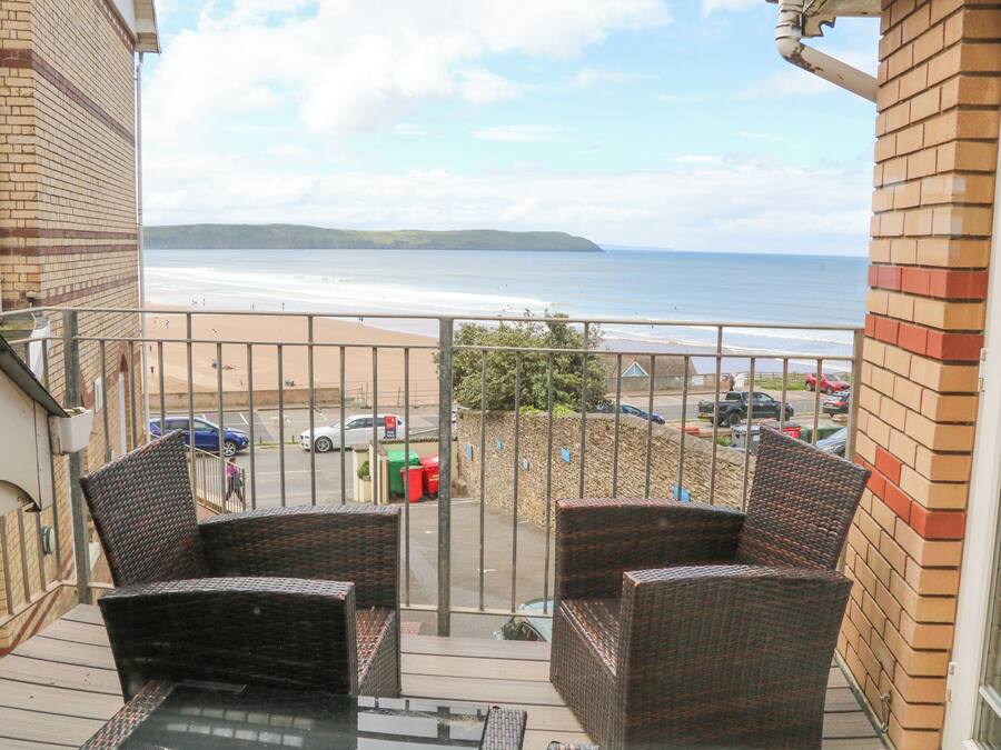 A balcony with wicker furniture overlooking a beach and parking area.