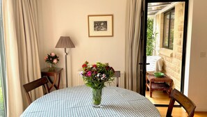 Un'area pranzo con un tavolo rotondo ricoperto da una tovaglia a quadri, un vaso con fiori, una lampada e un quadro appeso alla parete.
