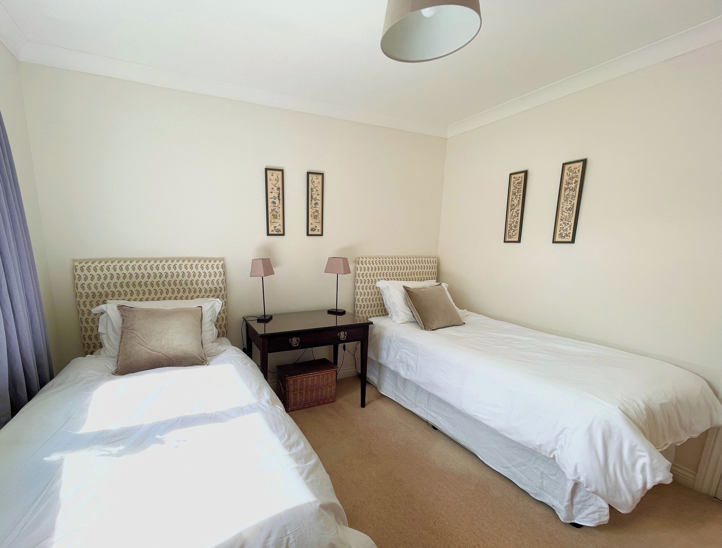 Ein Hotelzimmer mit zwei Einzelbetten, einem kleinen Schreibtisch mit Stuhl und einer Lampe.