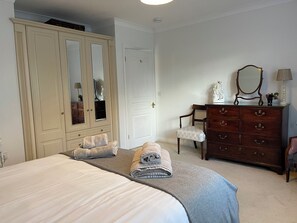A bedroom with a large bed, a wardrobe, a dresser, a chair, and a mirror. - 1A Erneston Crescent (Corsham)