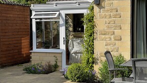 Una veranda con porta in vetro, recinzione in legno e un giardino con piante e fiori.