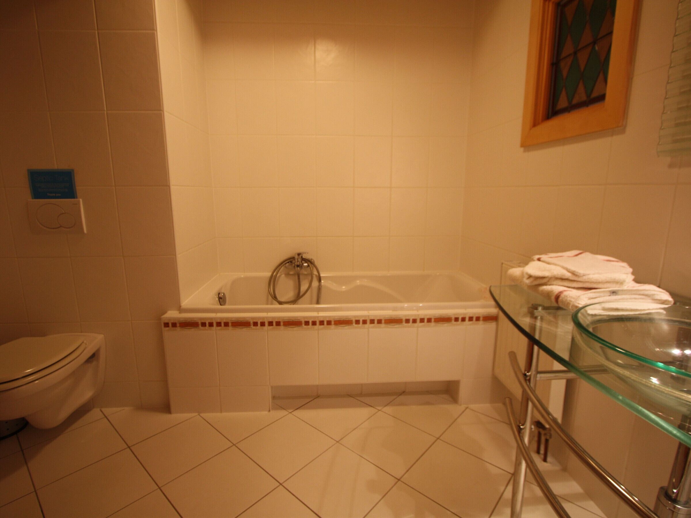 Een badkamer met een bad, toilet en een glazen wastafel.