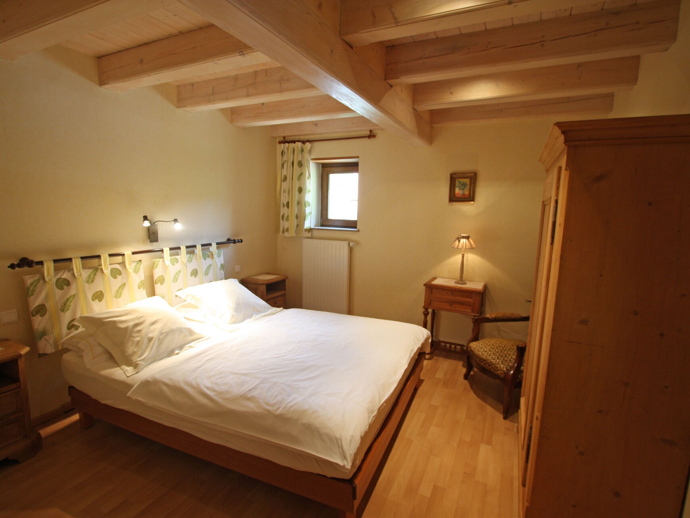 Un dormitorio con cama de madera, una mesita de noche, una lámpara, una ventana con cortinas y un armario de madera.